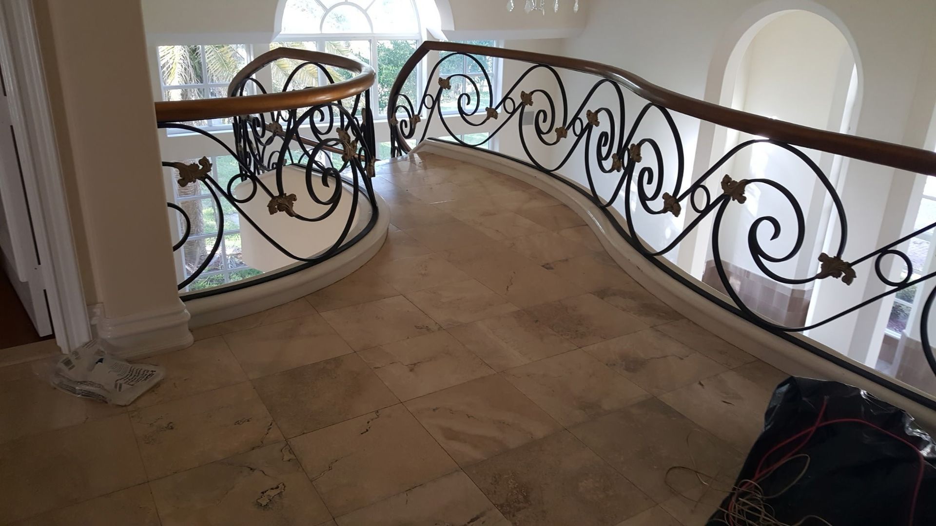 curved stairway landing with ornate black railing, wooden handrail, and beige tile floor