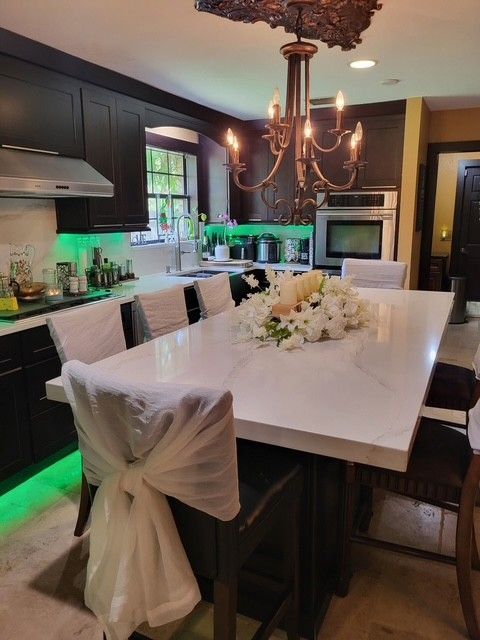 modern kitchen with a large white island, chandelier, and dark cabinets