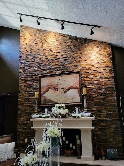 stone accent wall with track lighting, a fireplace, and a painting; decorated for a formal setting