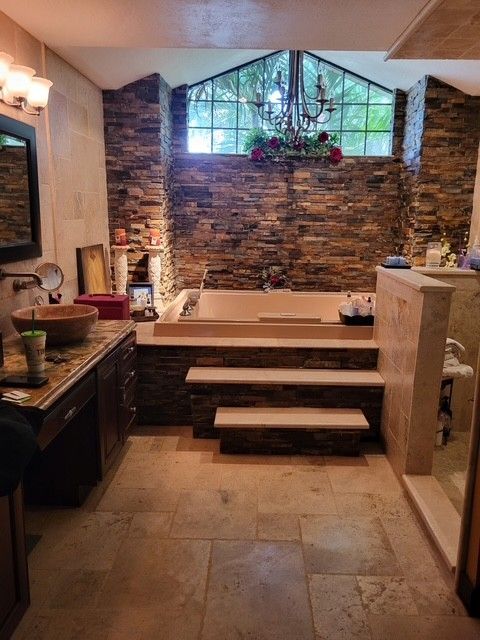 luxury bathroom with stone walls, sunken tub, and steps