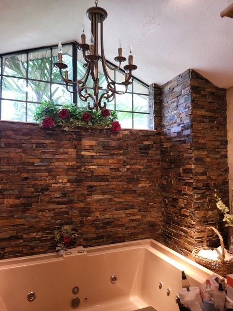 bathroom with stone accent walls, a chandelier, and a built-in jacuzzi tub
