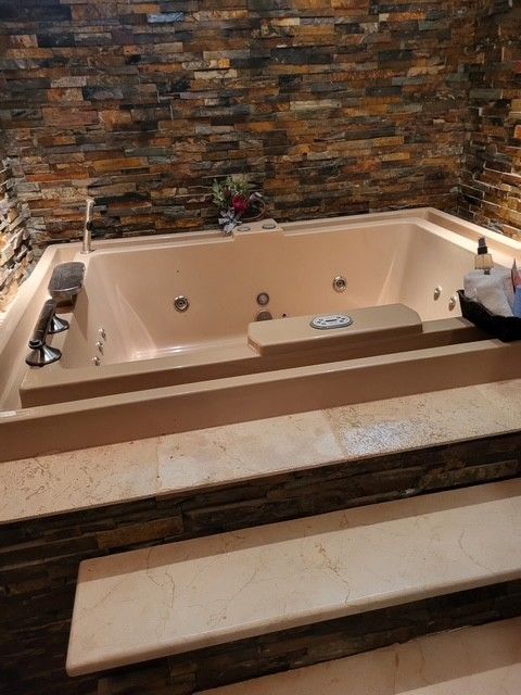 tan jacuzzi with jets built into stone steps, against a stone wall, and some supplies are in reach