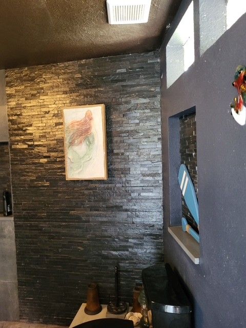 dark stone accent wall with artwork, next to a window with a decorative surfboard