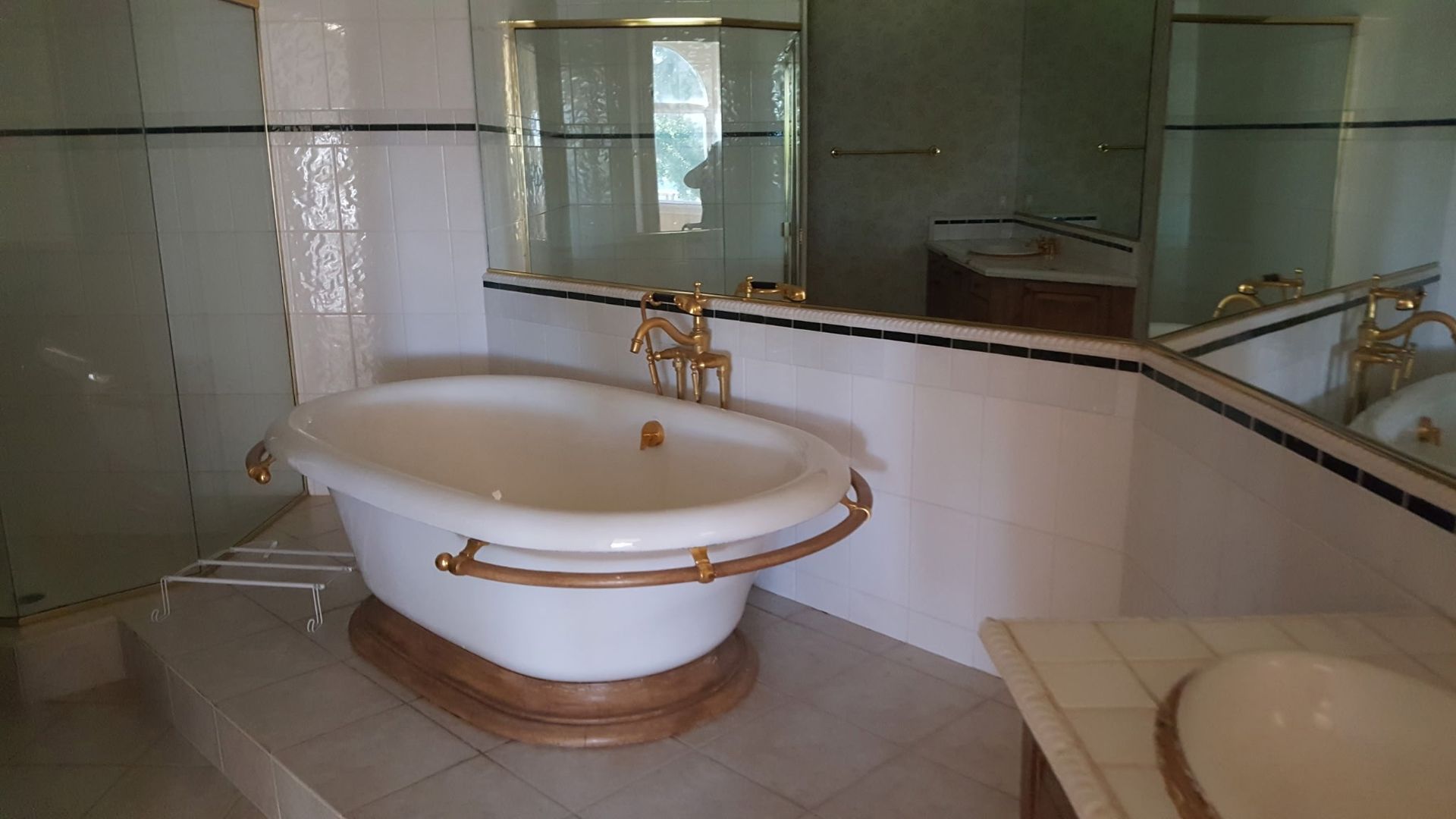 white clawfoot bathtub with gold fixtures in a bathroom, near a sink and a large mirror