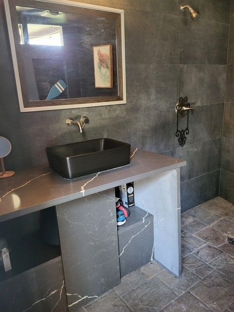 bathroom with gray tiled walls, black sink, and a large mirror
