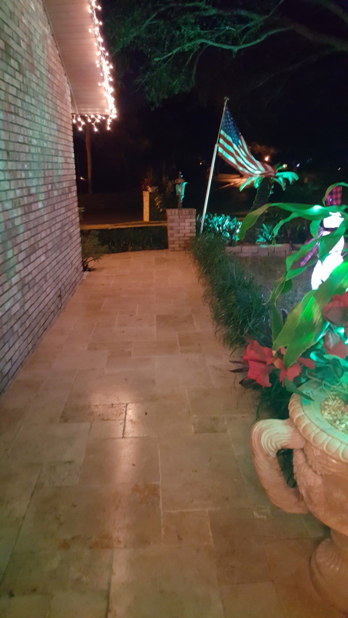 lit walkway beside a brick house, US flag flies, and Christmas lights are visible