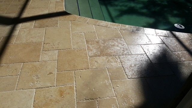beige stone tile pool deck with dark green water and shadows