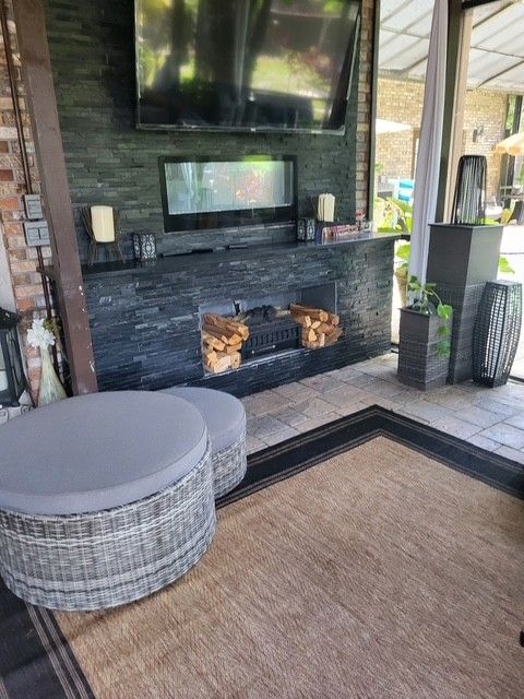 outdoor seating area with fireplace, TV, rug, gray wicker furniture, black stone fireplace surround