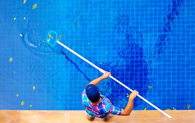 Person cleaning a blue tiled pool with a long pole, viewed from above