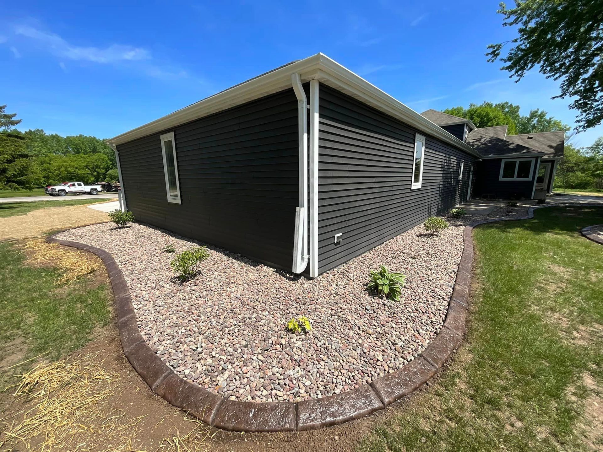 A black house with a concrete curb and gravel in front of it.