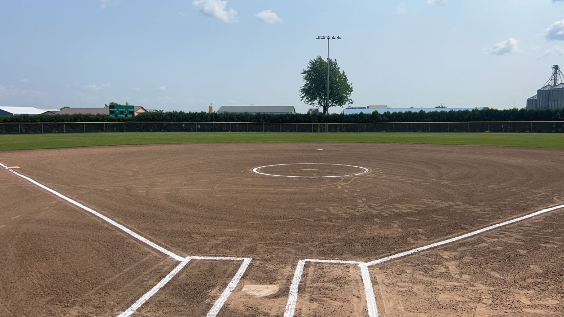 A baseball field with a fence and a tree in the background.