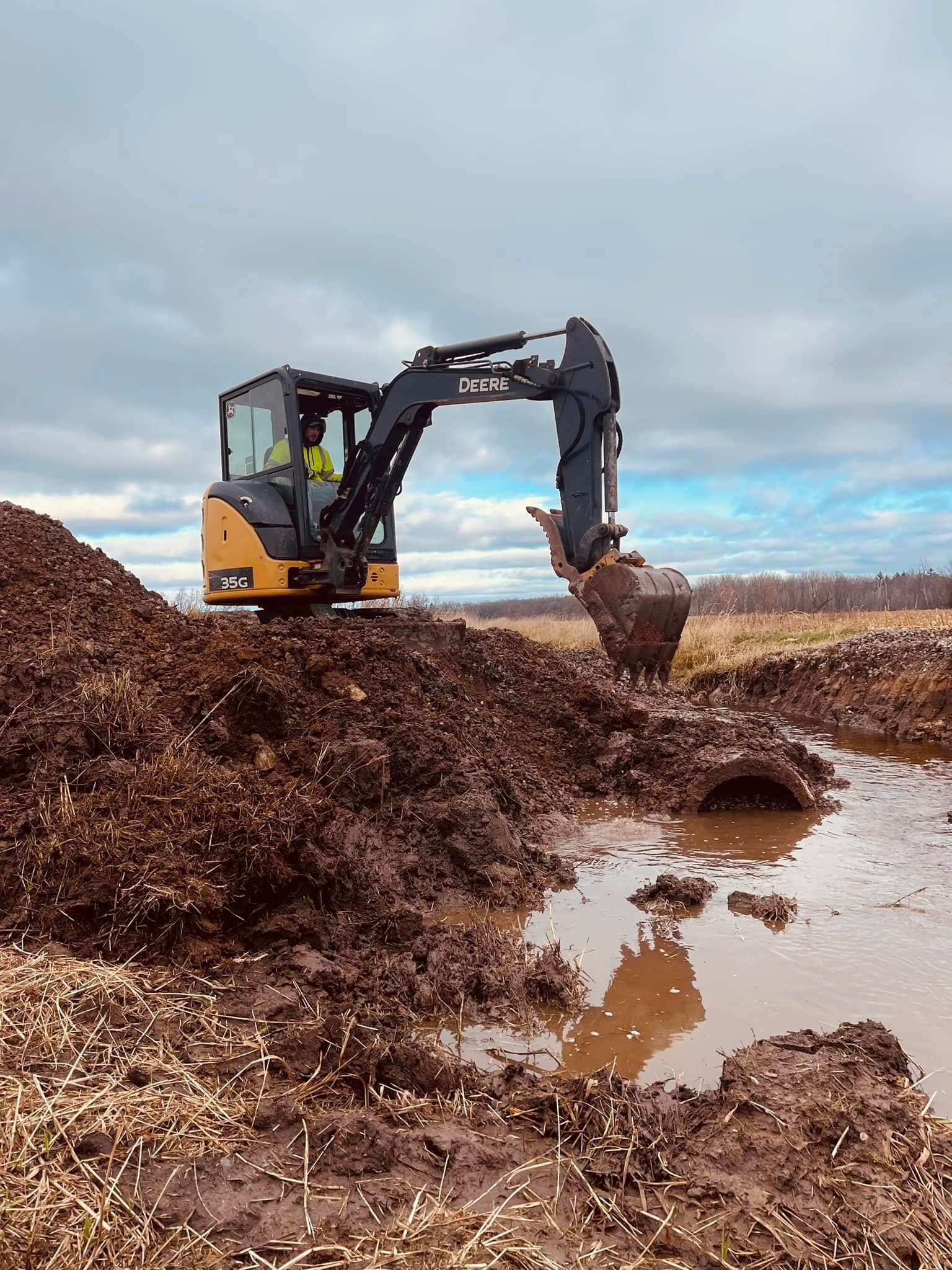 An excavator is digging a hole in the mud in a muddy field.