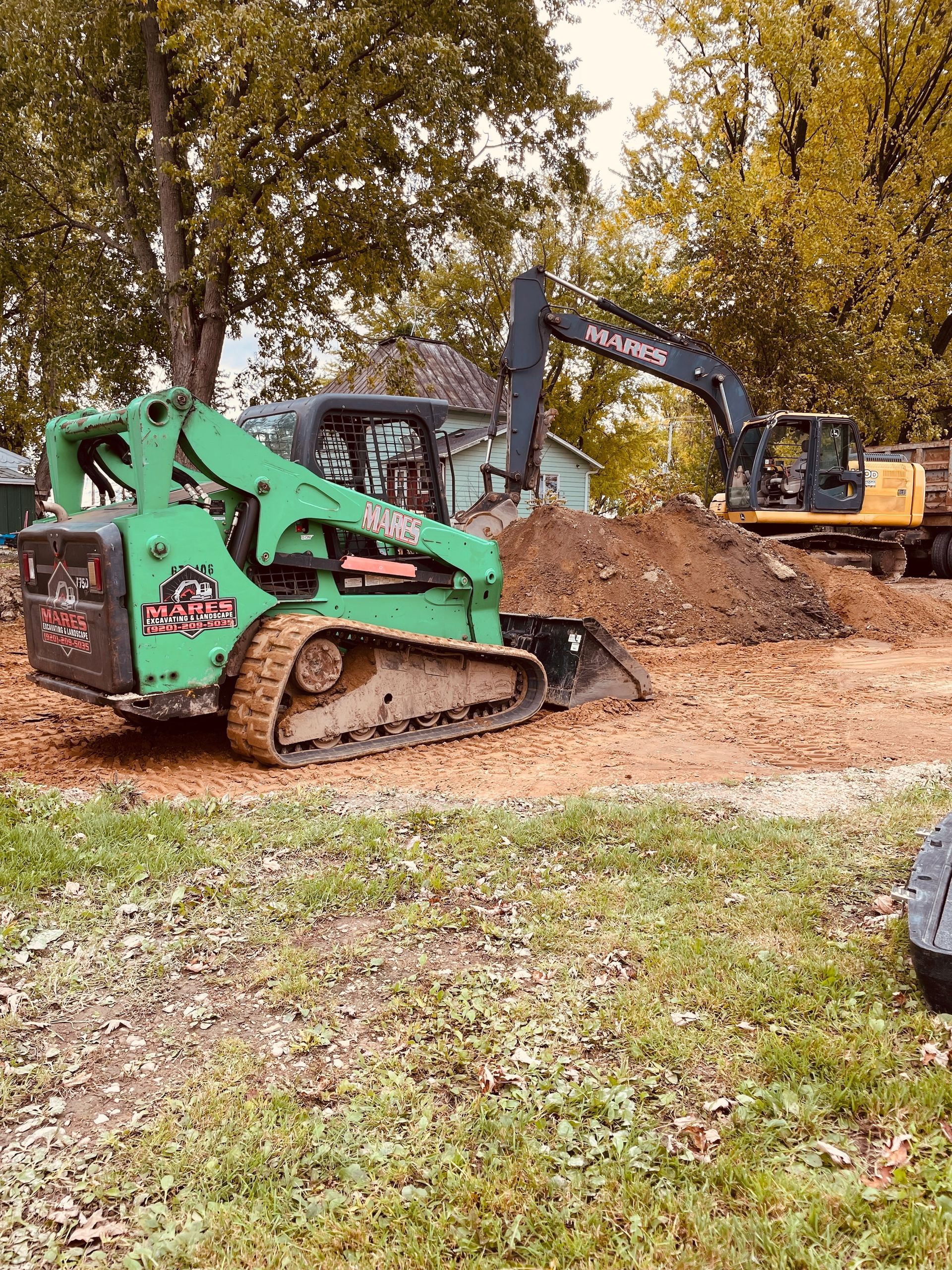 A green bulldozer is digging a hole in the dirt next to a yellow excavator.