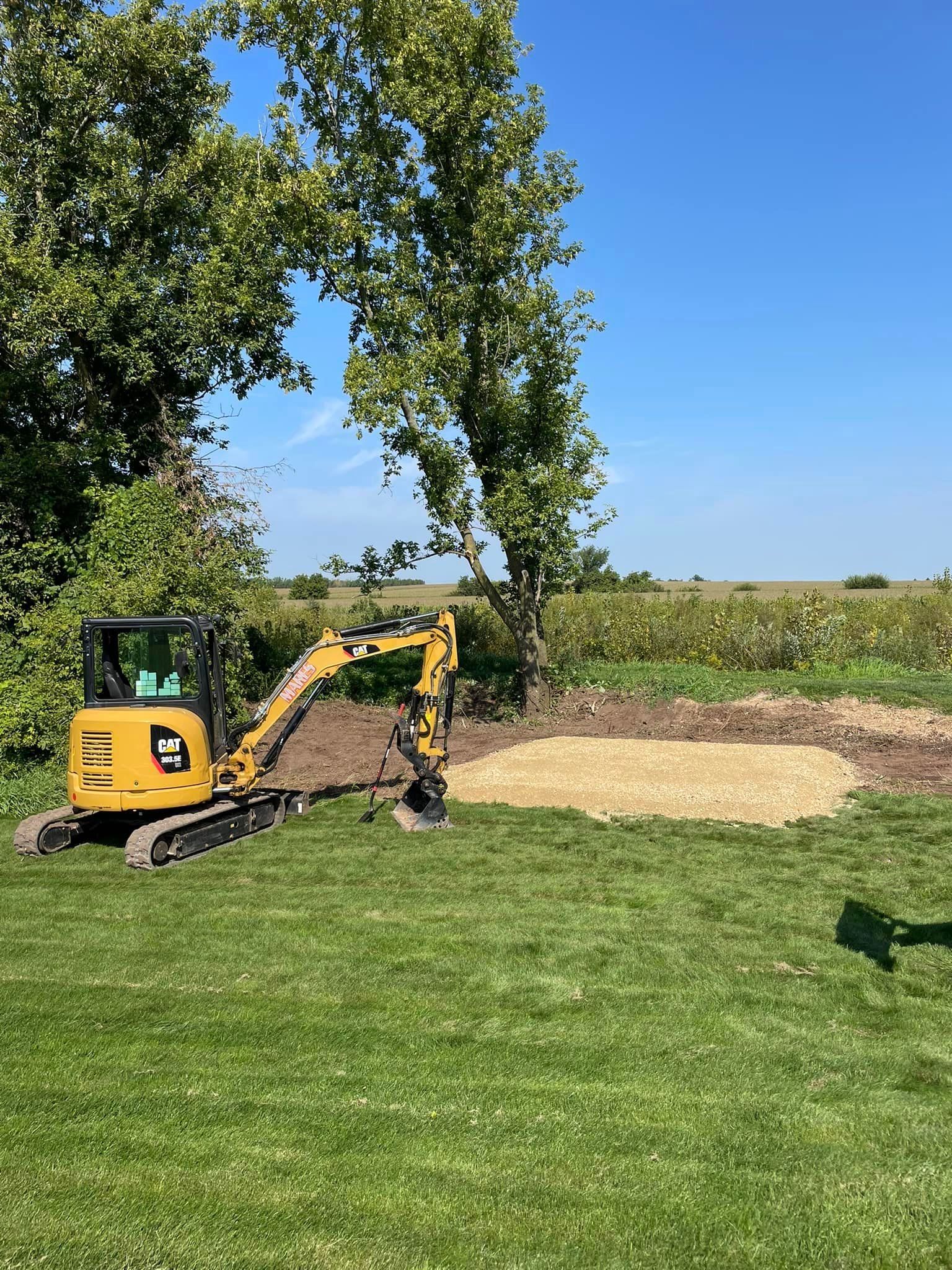 A yellow excavator is digging a hole in the grass.