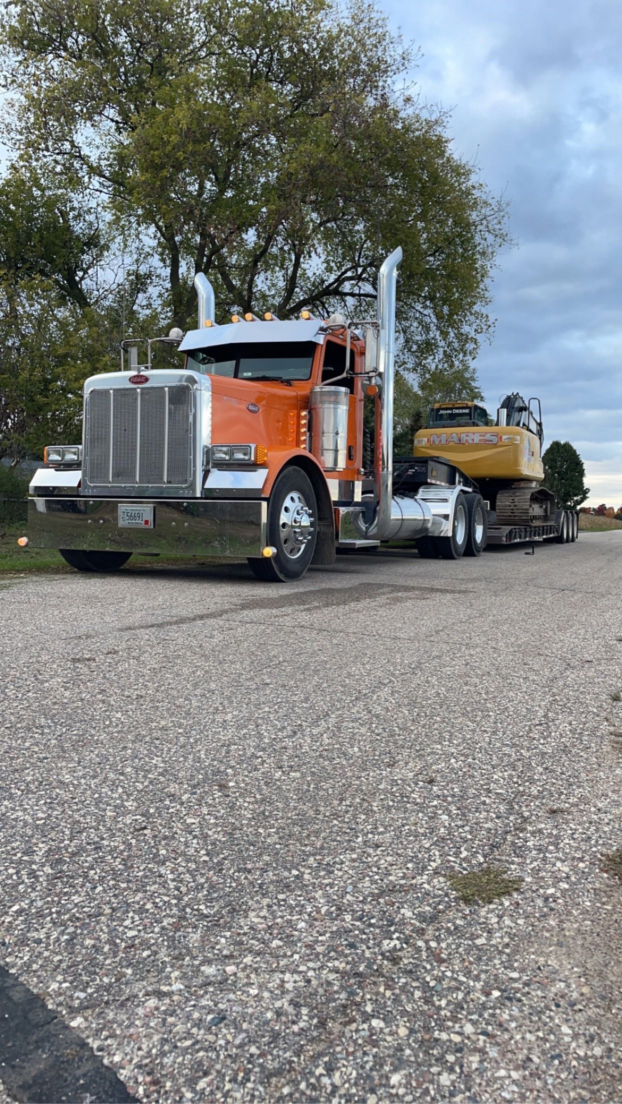 An orange semi truck is parked on the side of the road next to a yellow excavator.
