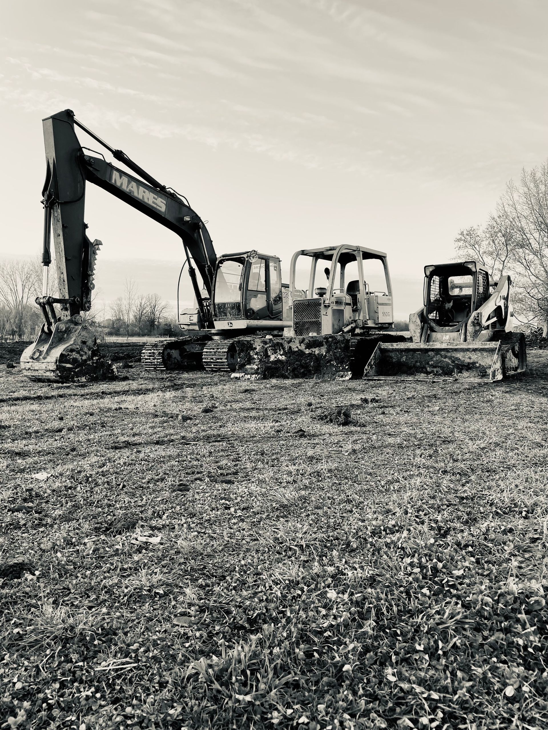 A black and white photo of two construction vehicles in a field.