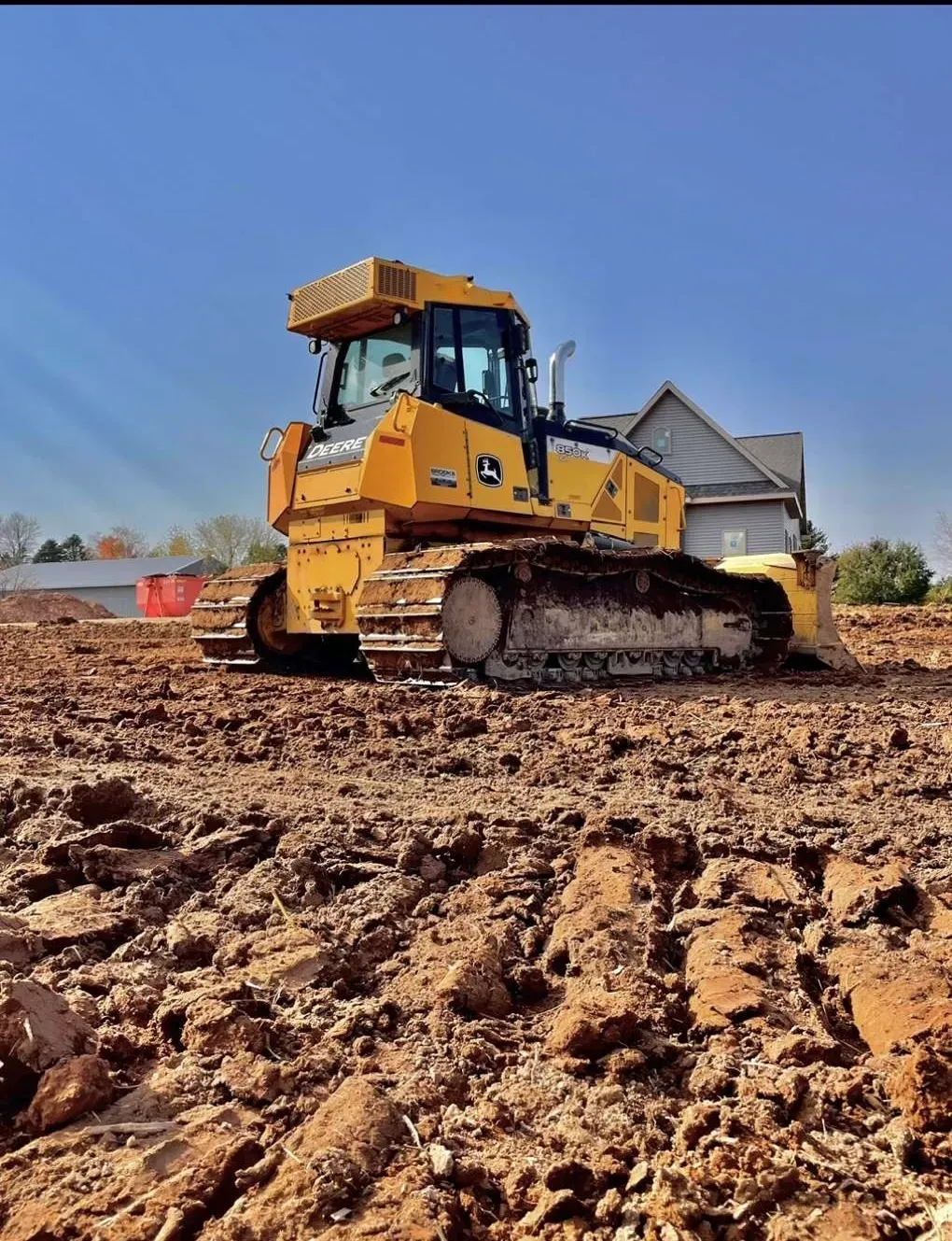 A yellow bulldozer is plowing a dirt field in front of a house.