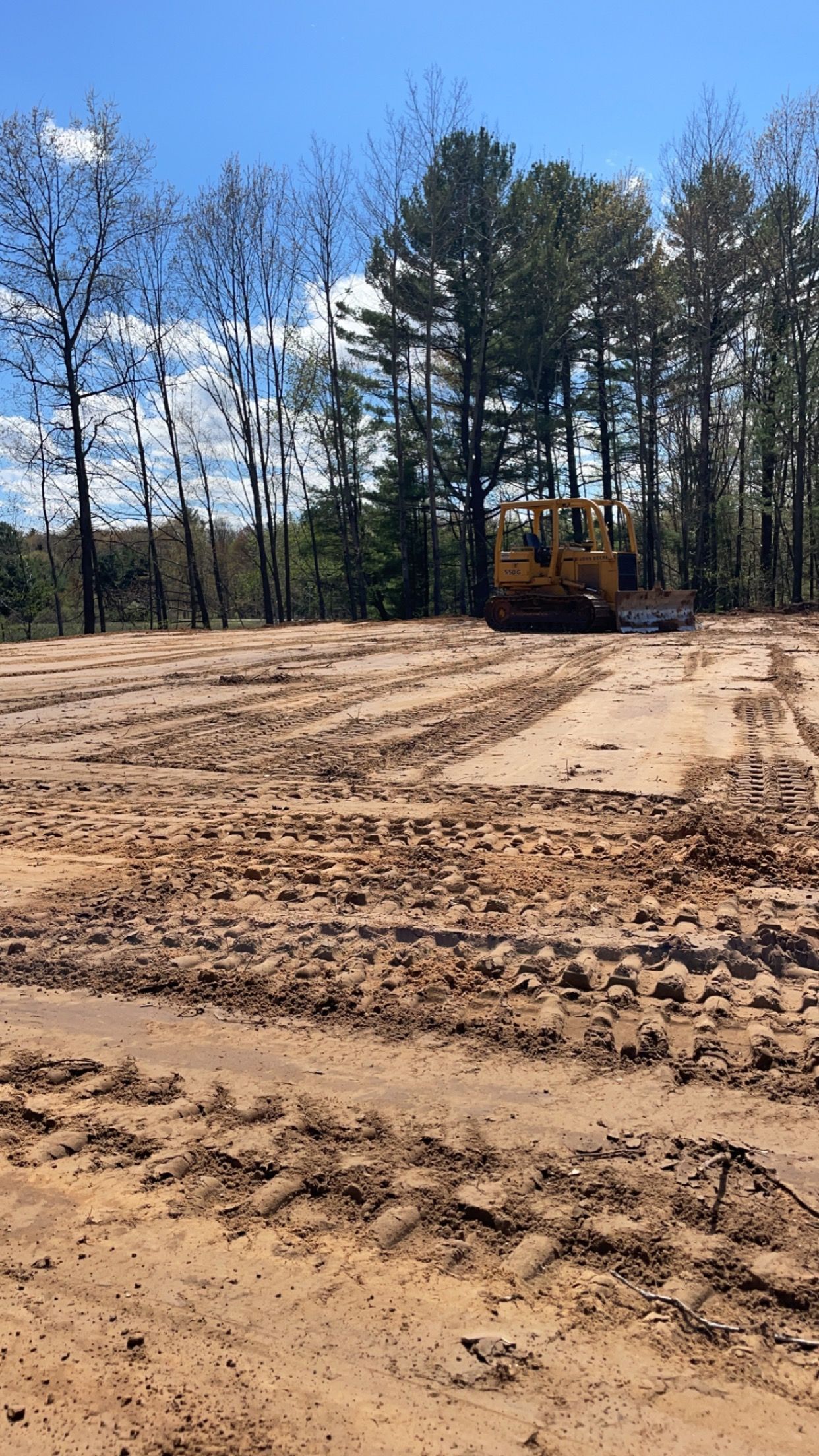 A bulldozer is moving dirt in a field with trees in the background.