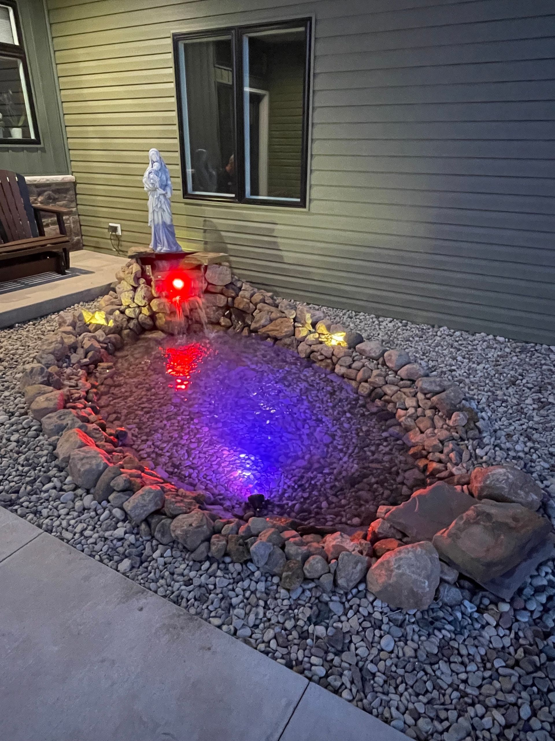 There is a fountain in the middle of the rocks in front of a house.