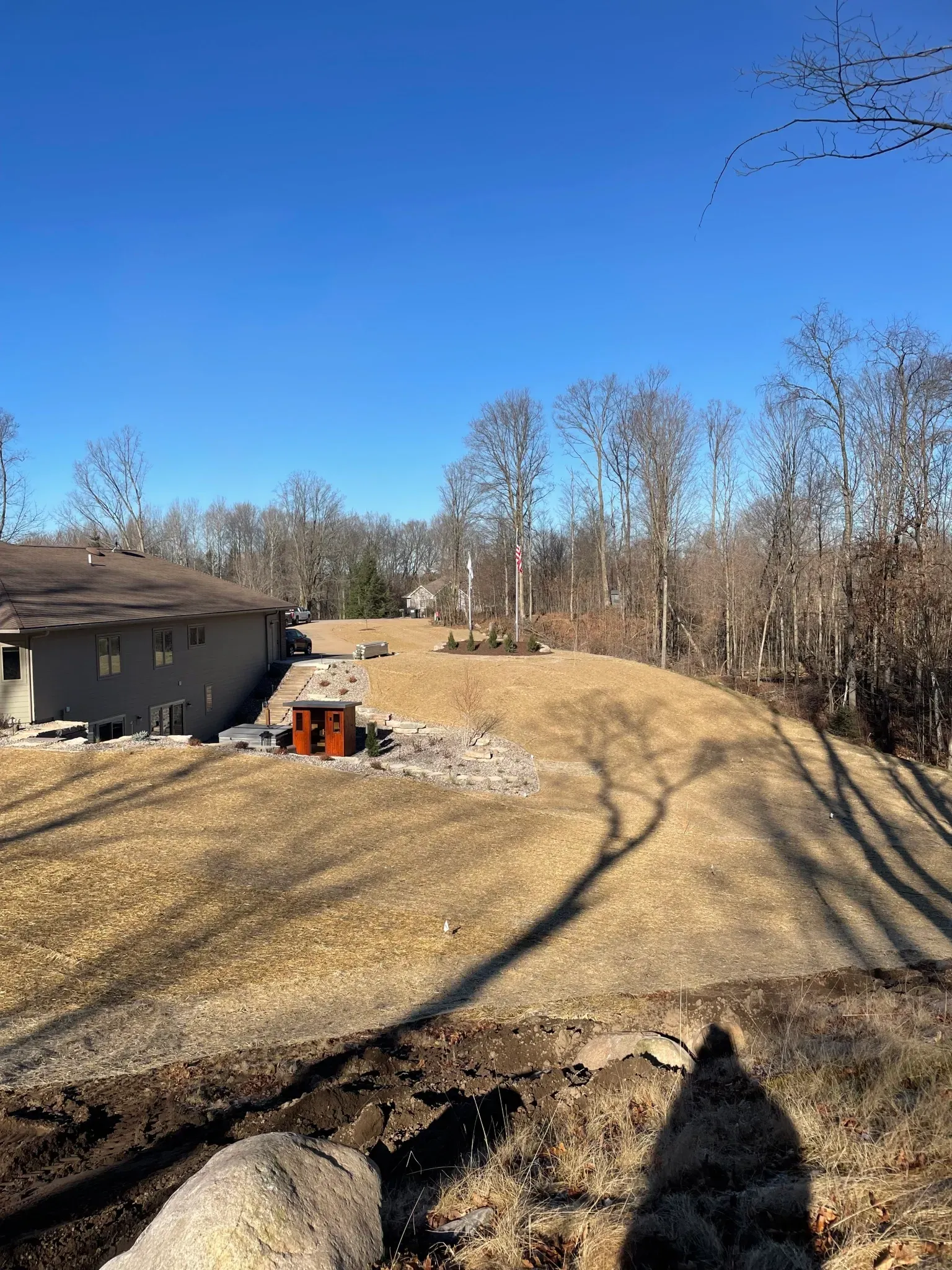 A shadow of a person is cast on a dirt road in front of a house.