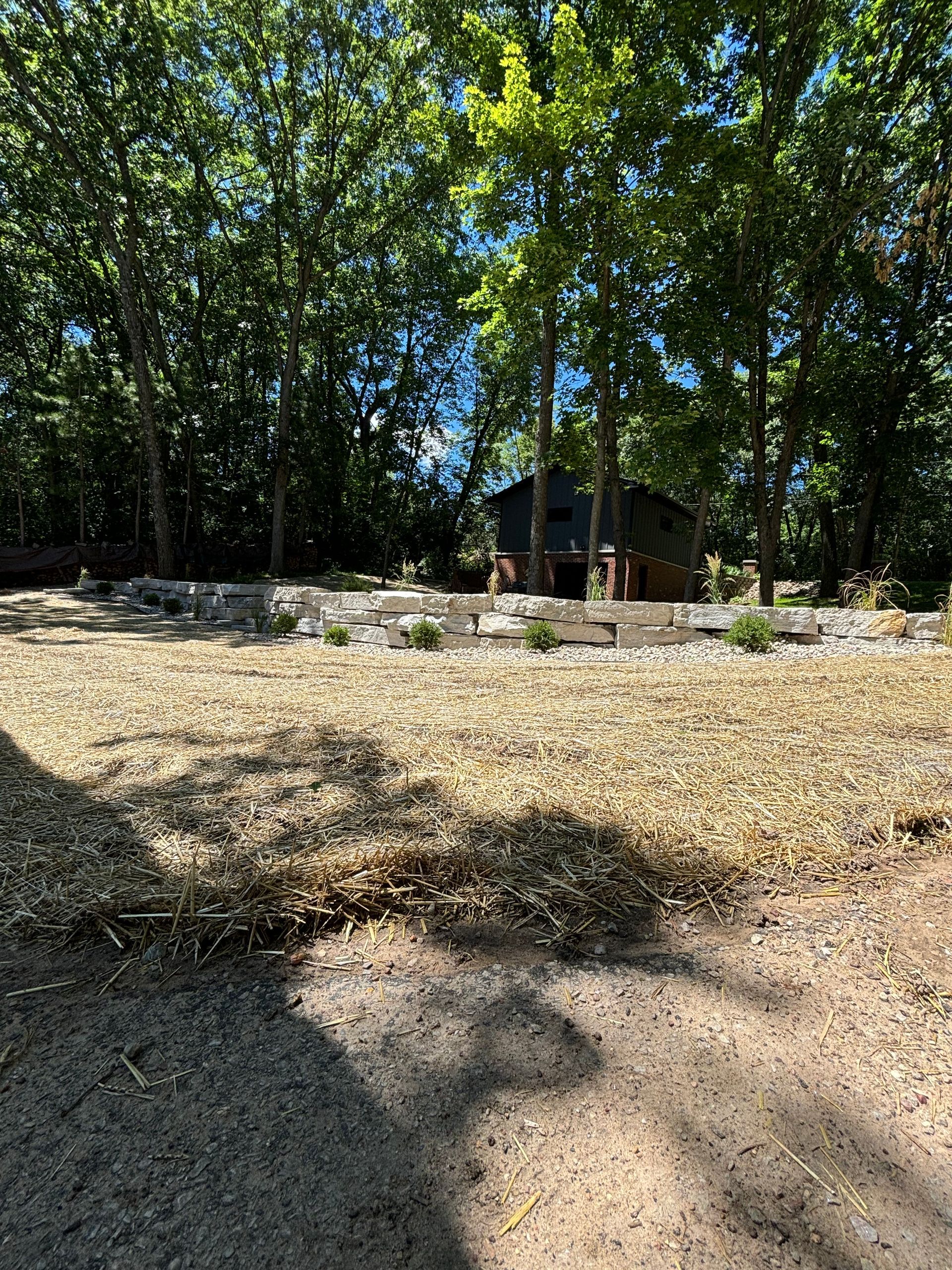 A dirt field with trees in the background and a house in the background.
