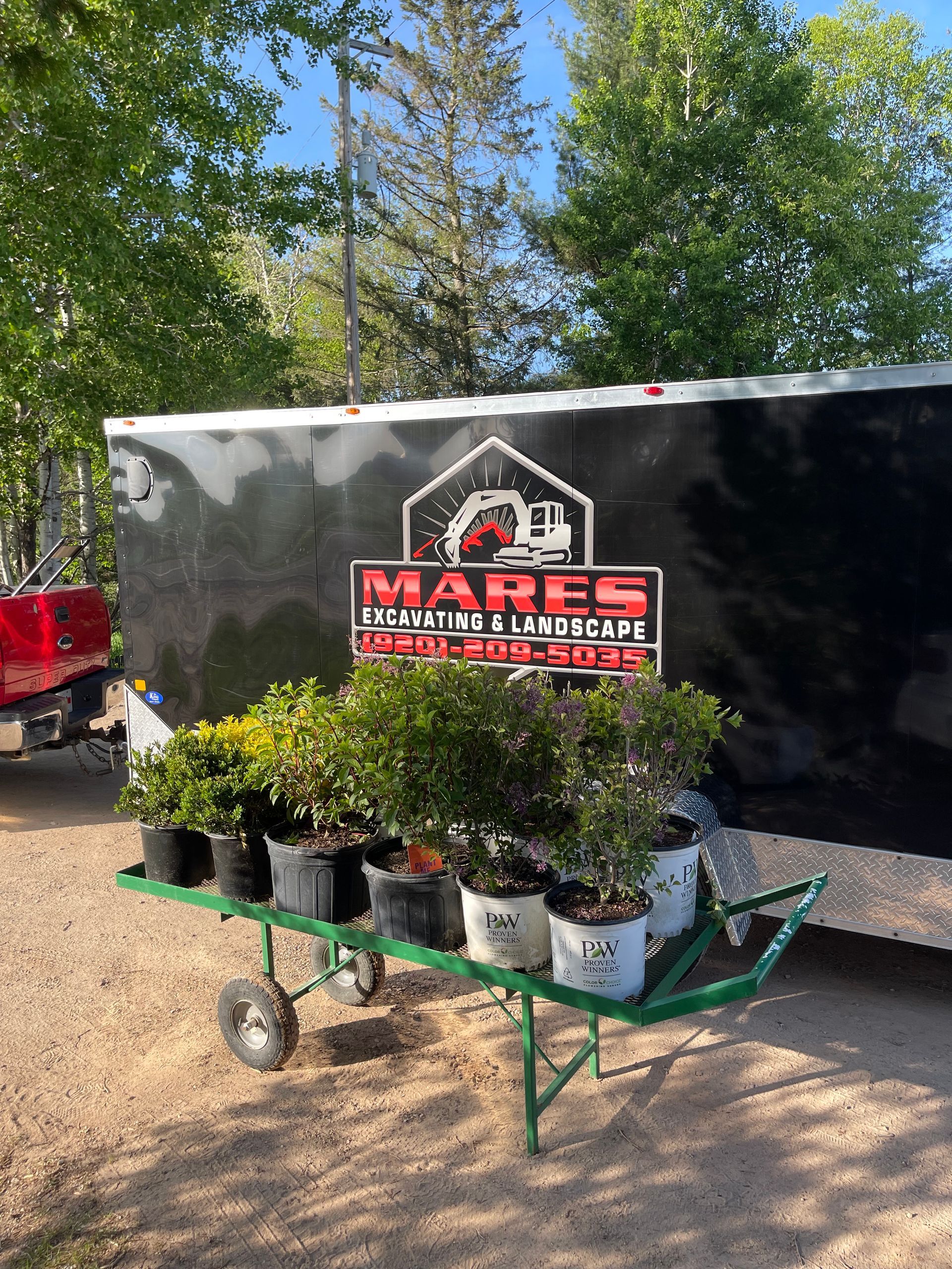 A cart filled with potted plants is in front of a trailer.