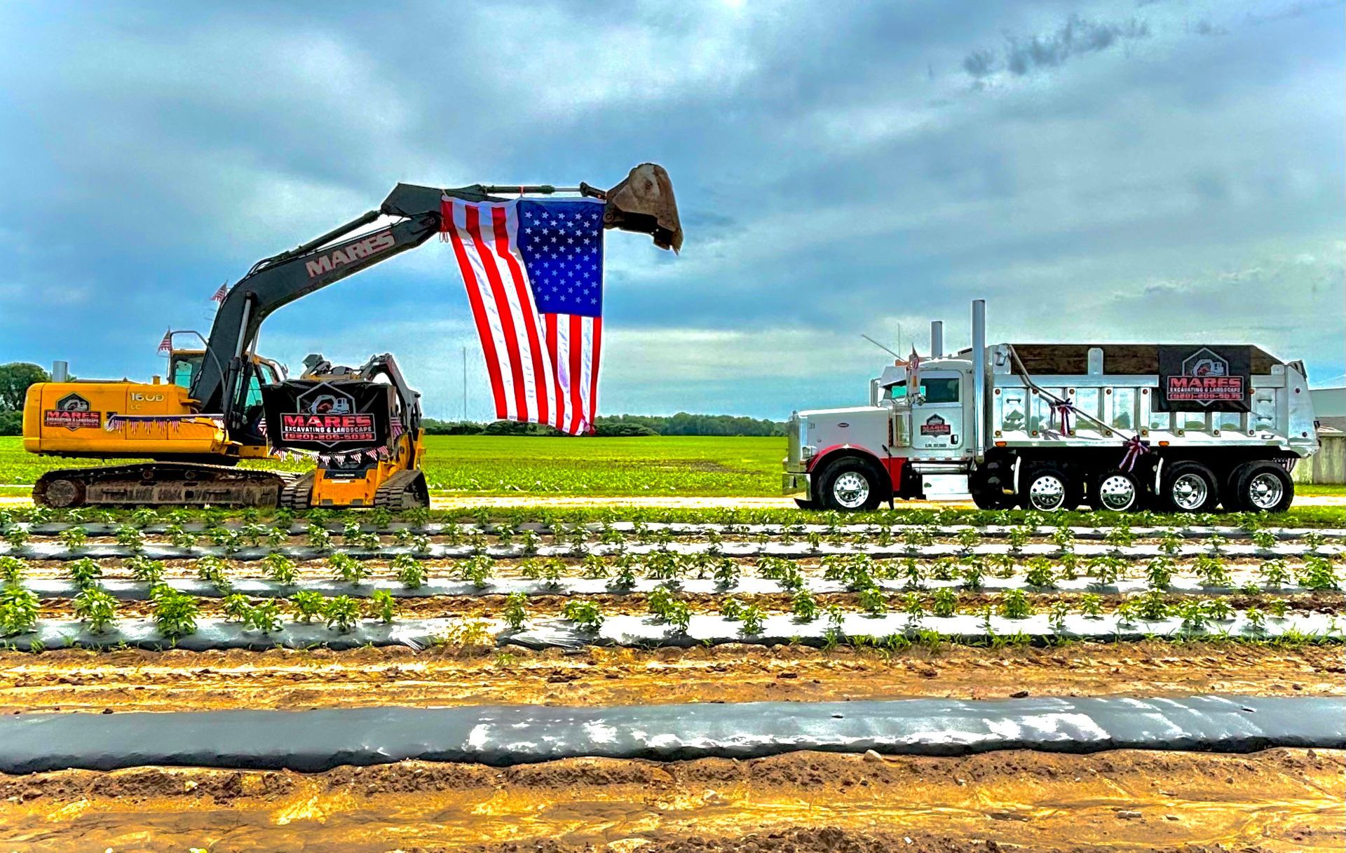 A truck is driving through a field with an american flag in the background.