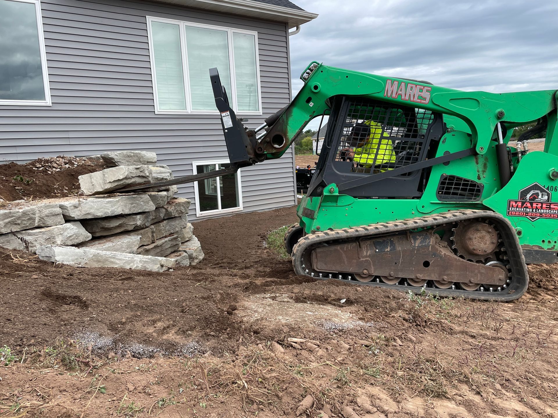 A green bulldozer is moving dirt in front of a house.