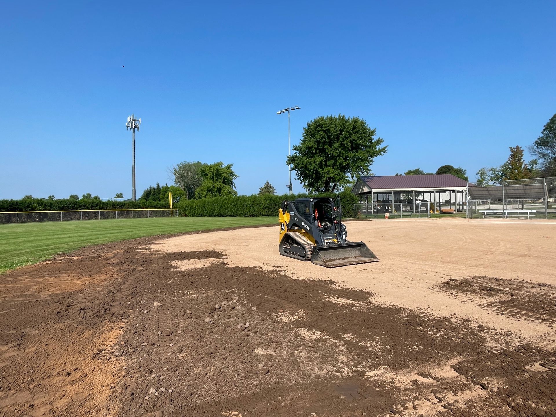 A bulldozer is moving dirt on a baseball field.
