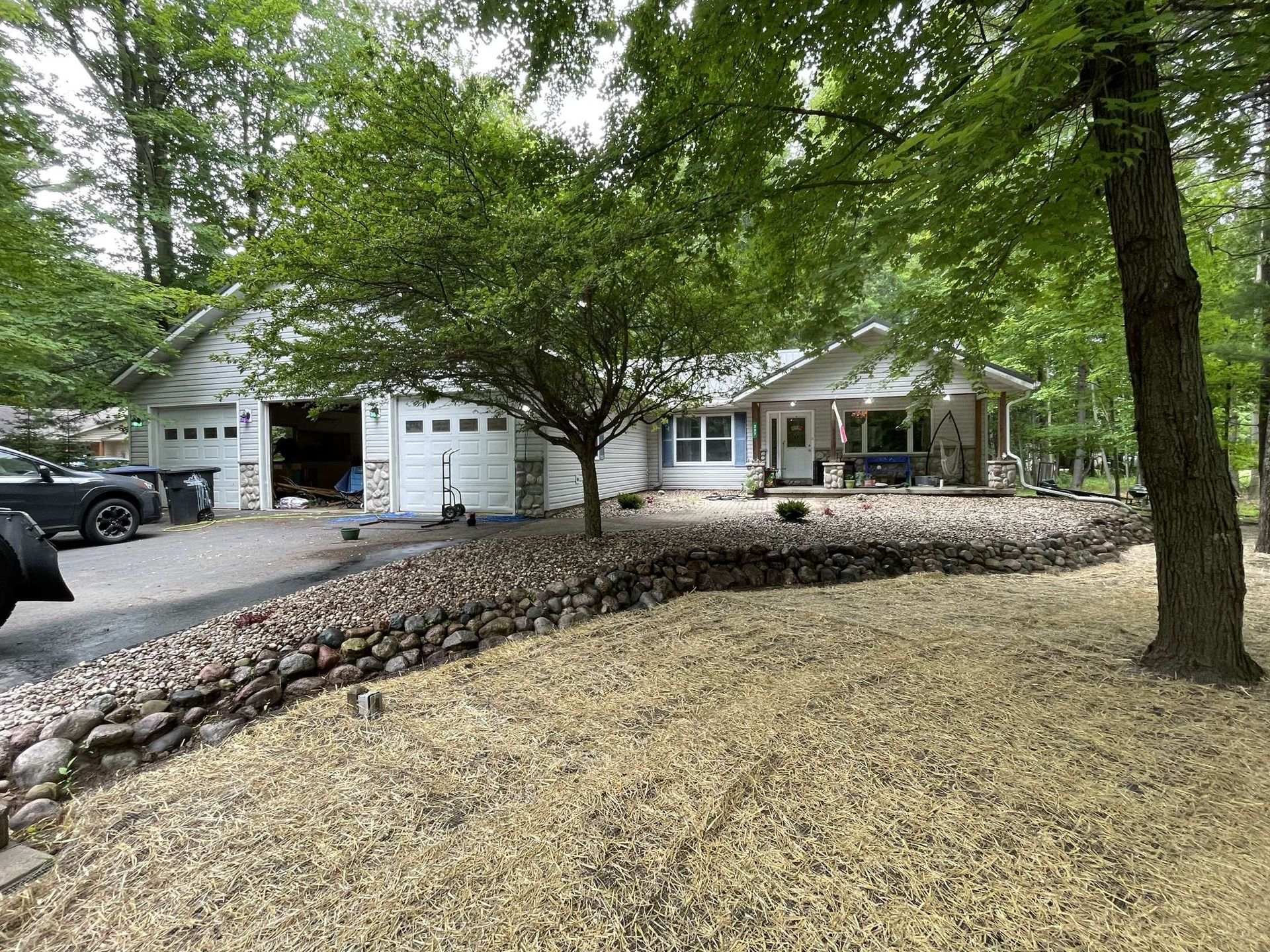 A truck is parked in front of a white house surrounded by trees.