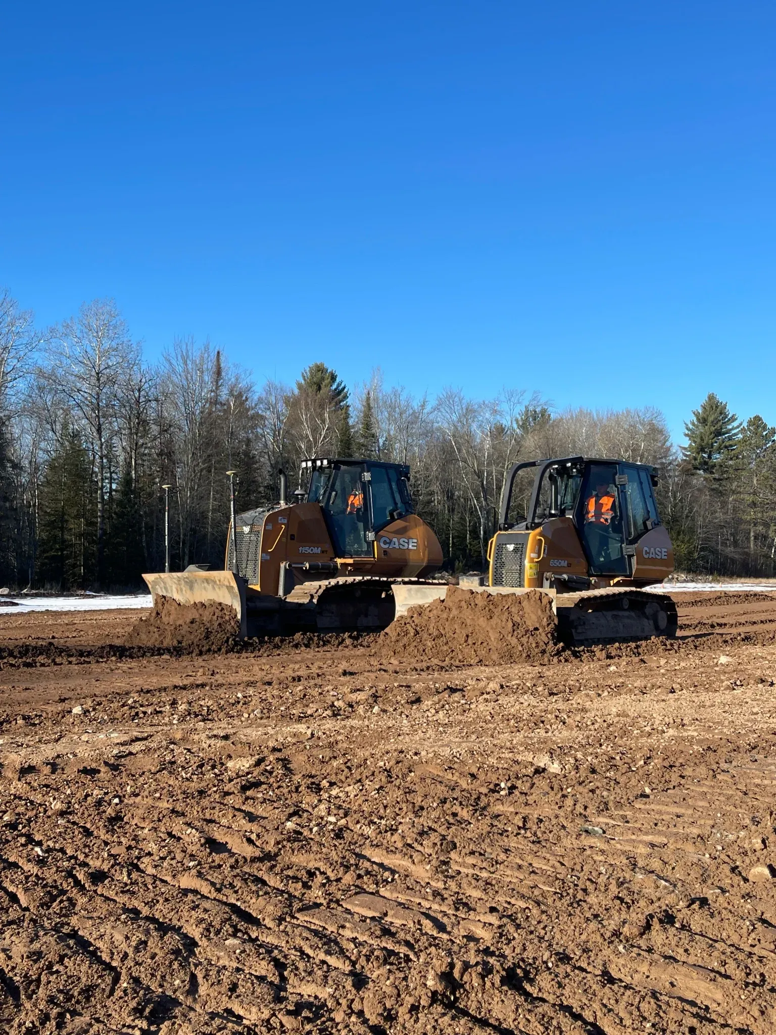 Two bulldozers are working on a dirt field.