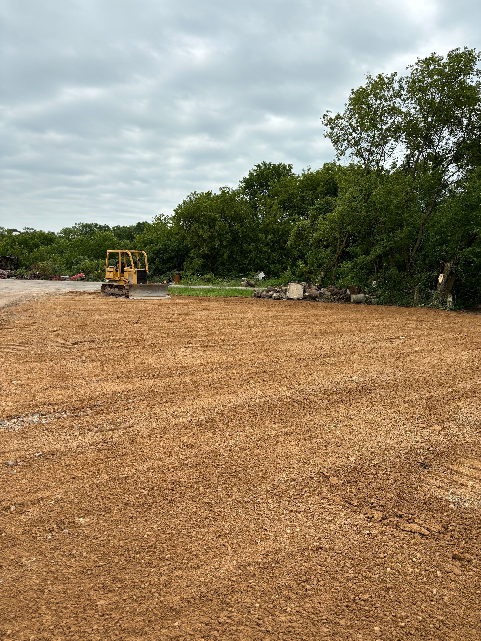 A bulldozer is moving dirt in a field with trees in the background.