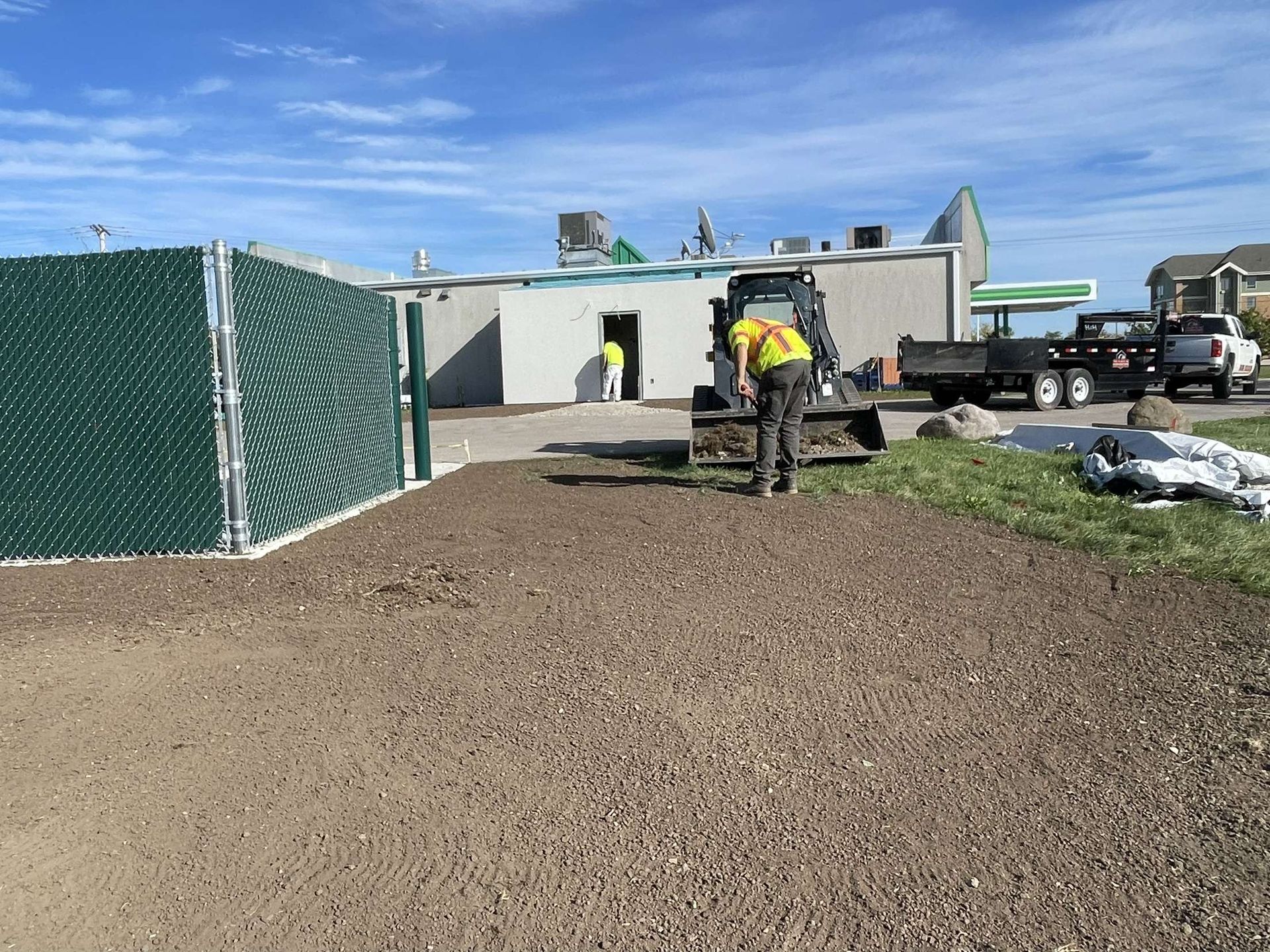 A man is working on a gravel driveway in front of a building.