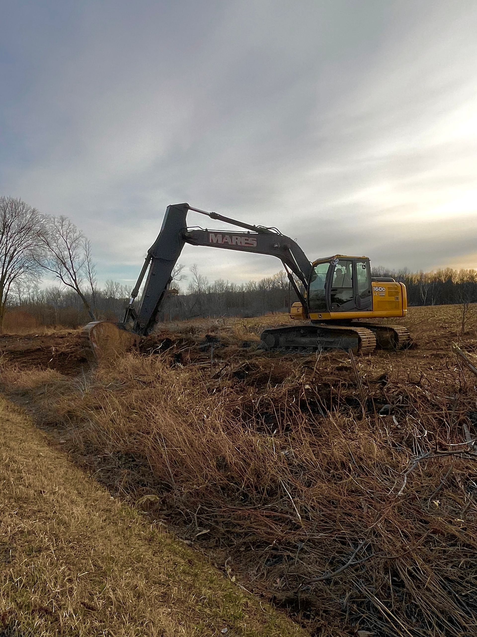 A large yellow excavator is digging a hole in a field.