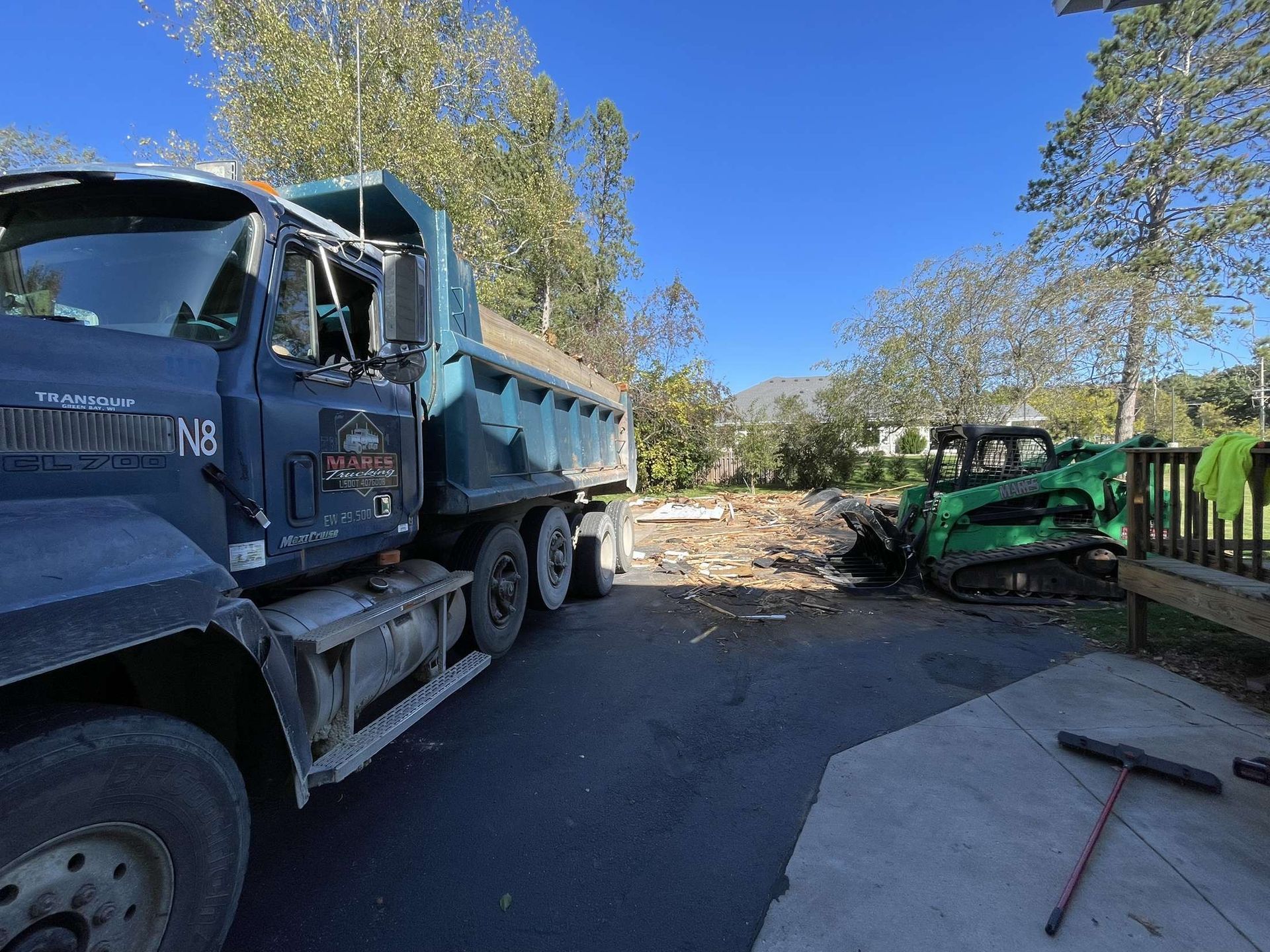 A dump truck is parked on the side of the road next to a tractor.