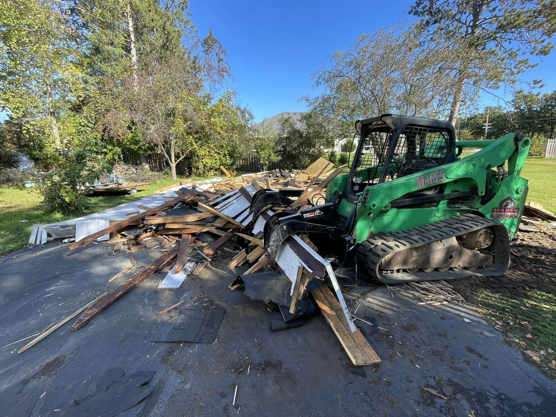 A green bulldozer is sitting on the side of a road next to a pile of wood.