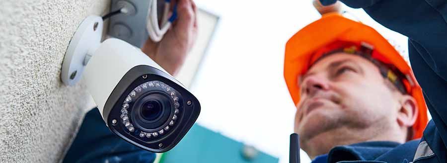 A man is installing a security camera on a wall.