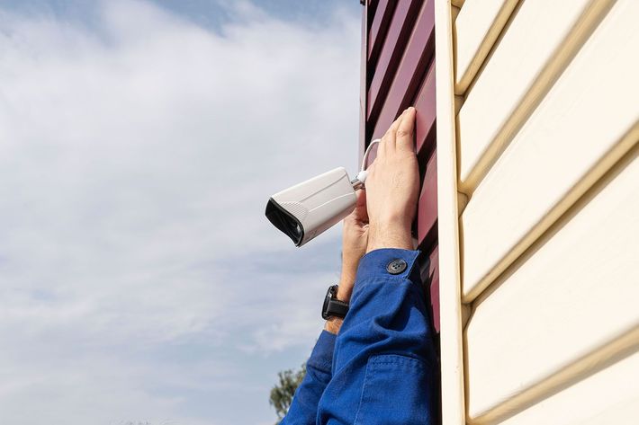 A person is installing a security camera on the side of a building