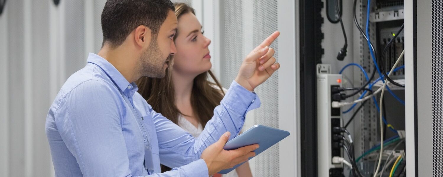 A man and a woman are looking at a tablet in a server room.