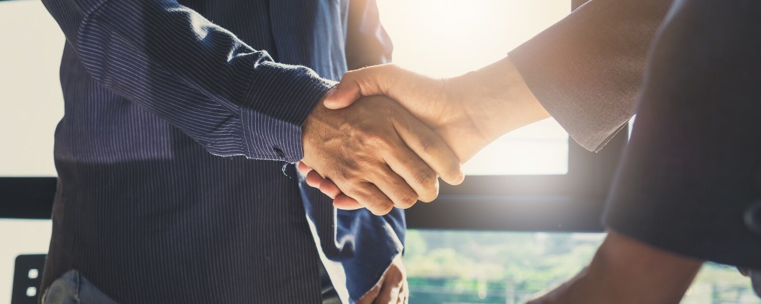 Two business people are shaking hands in front of a window.