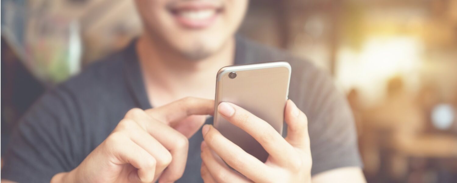 A man is holding a cell phone in his hands and smiling.