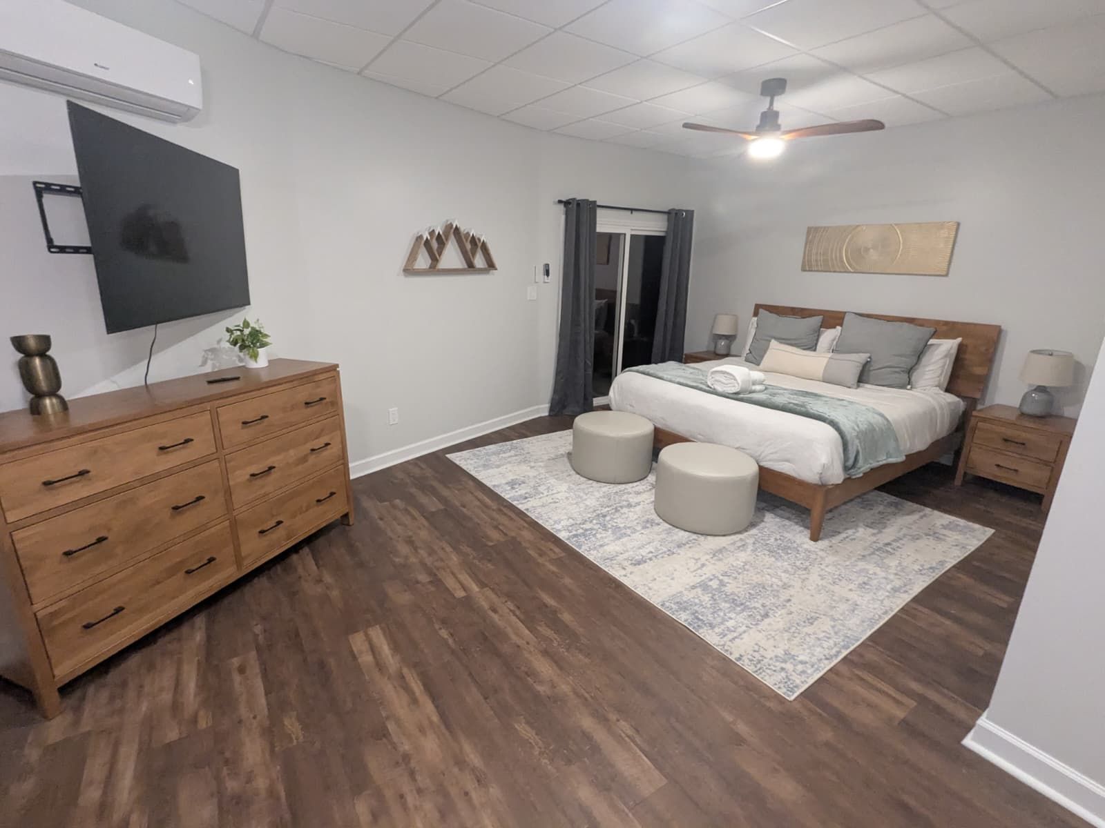 Bedroom with wooden furniture, a bed, TV, and rug on a dark wood floor.