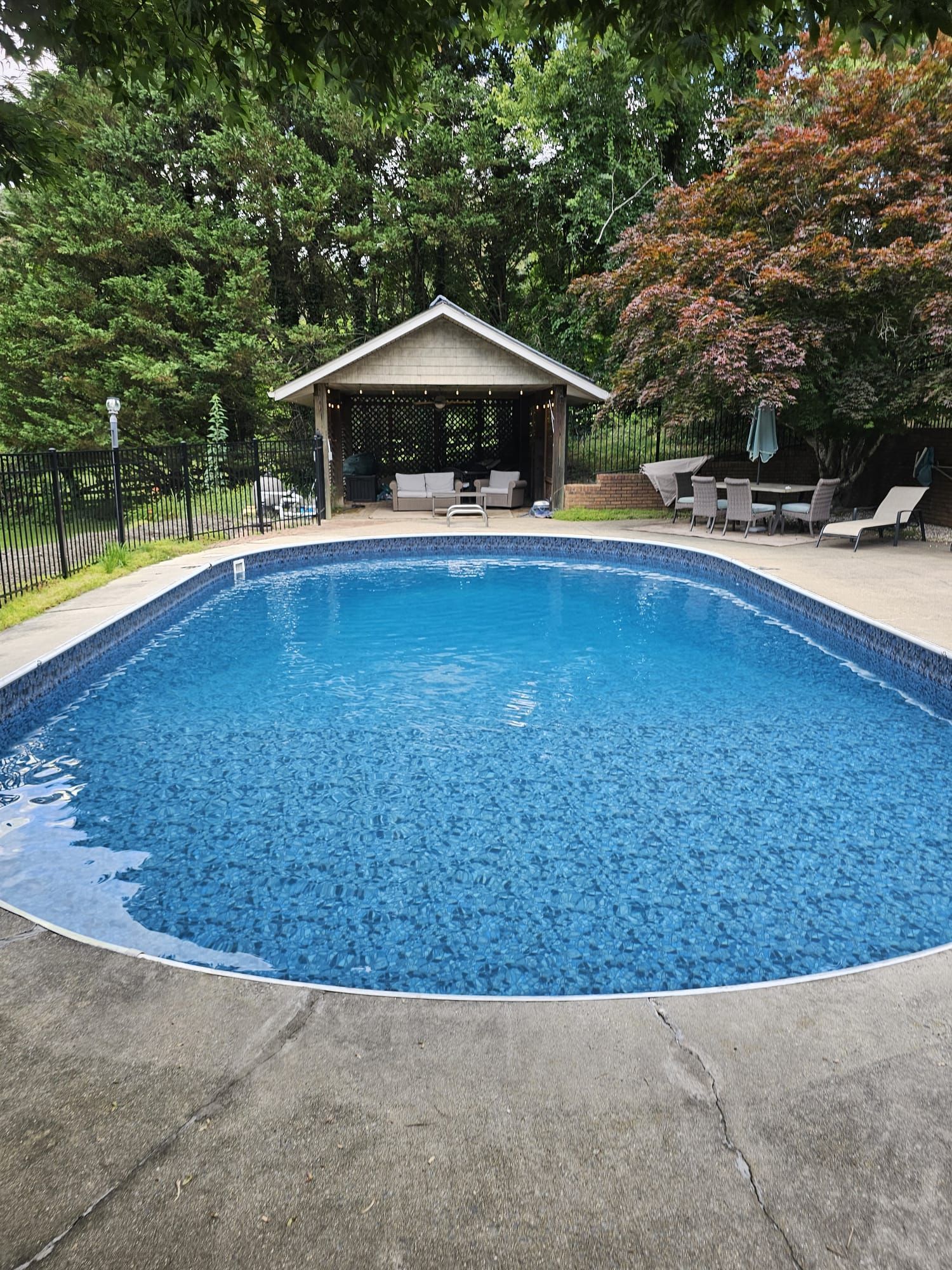 Pool with blue tile, patio, gazebo, trees, and lounge chairs.