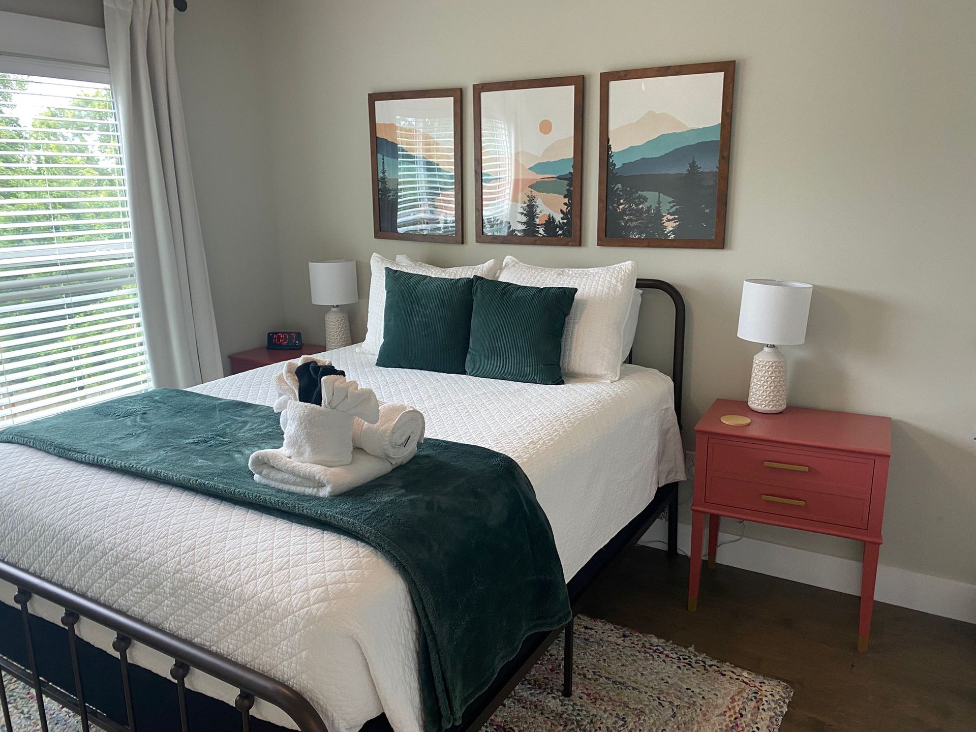 Bedroom with white bedding, dark green accents, framed landscape art, and a red nightstand.