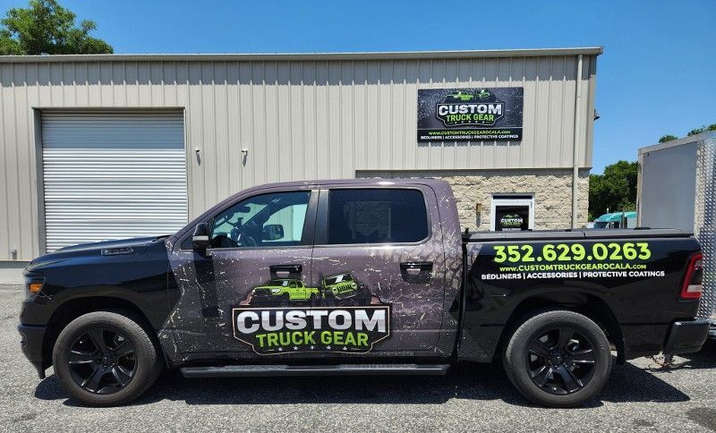 A black truck is parked in front of a building that says custom truck gear.