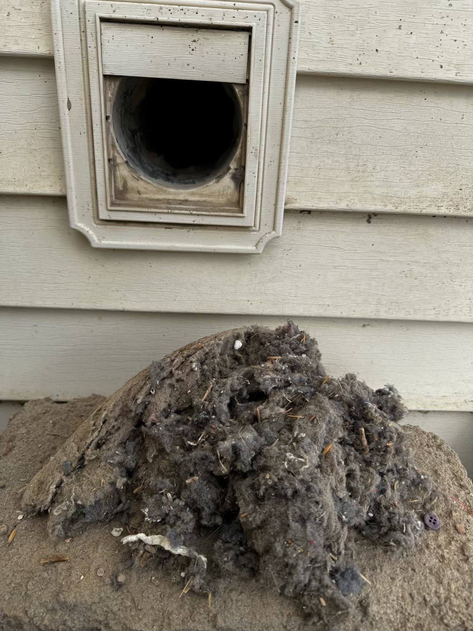 Exterior dryer vent with large pile of lint below.