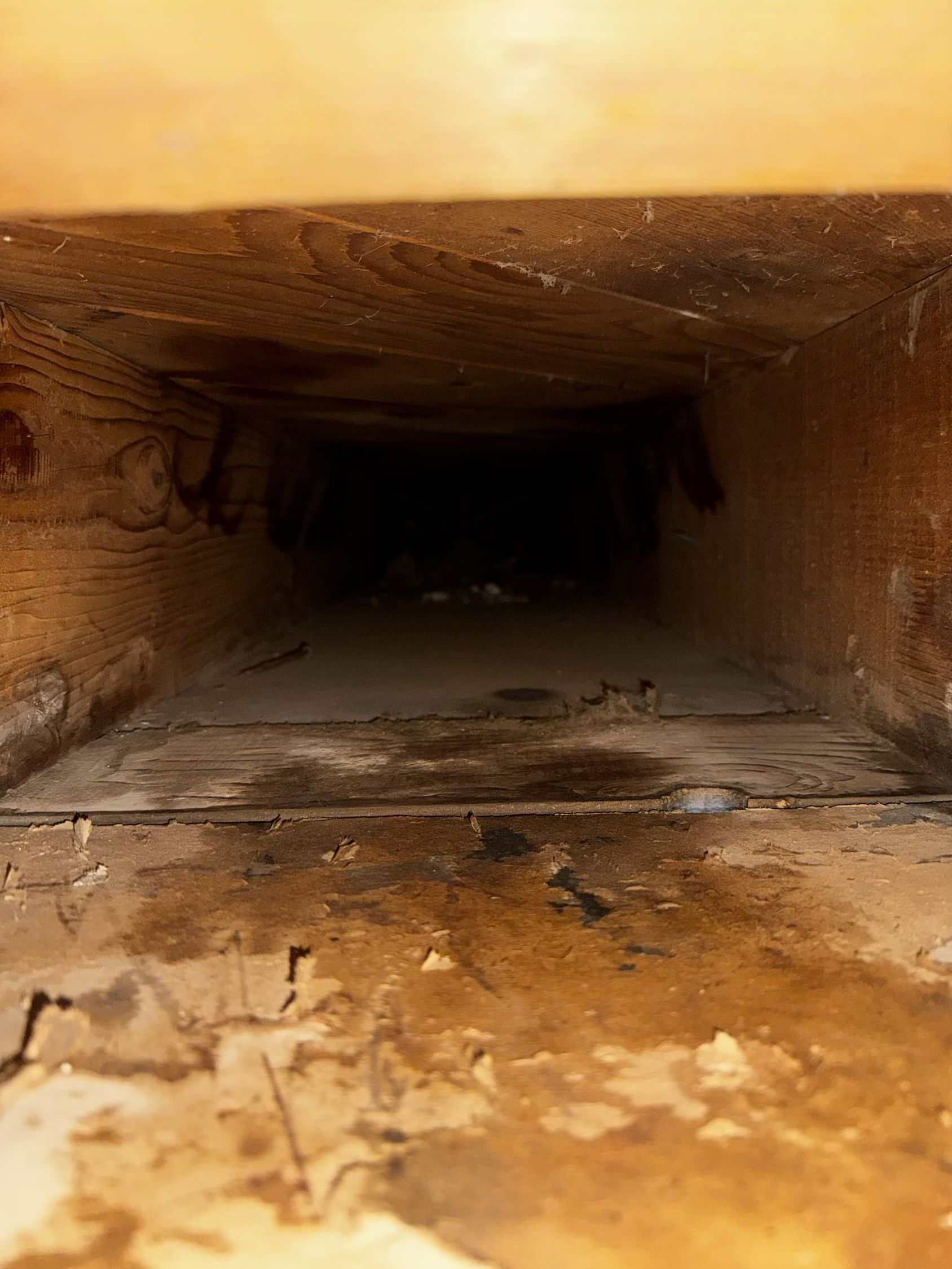 Inside view of a rectangular, dark, dirty air duct with visible stains and debris.