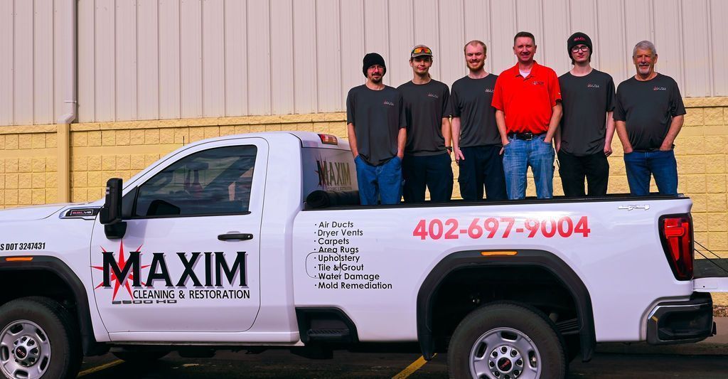 Group of six men standing in the back of a white Maxim truck, phone number on side.