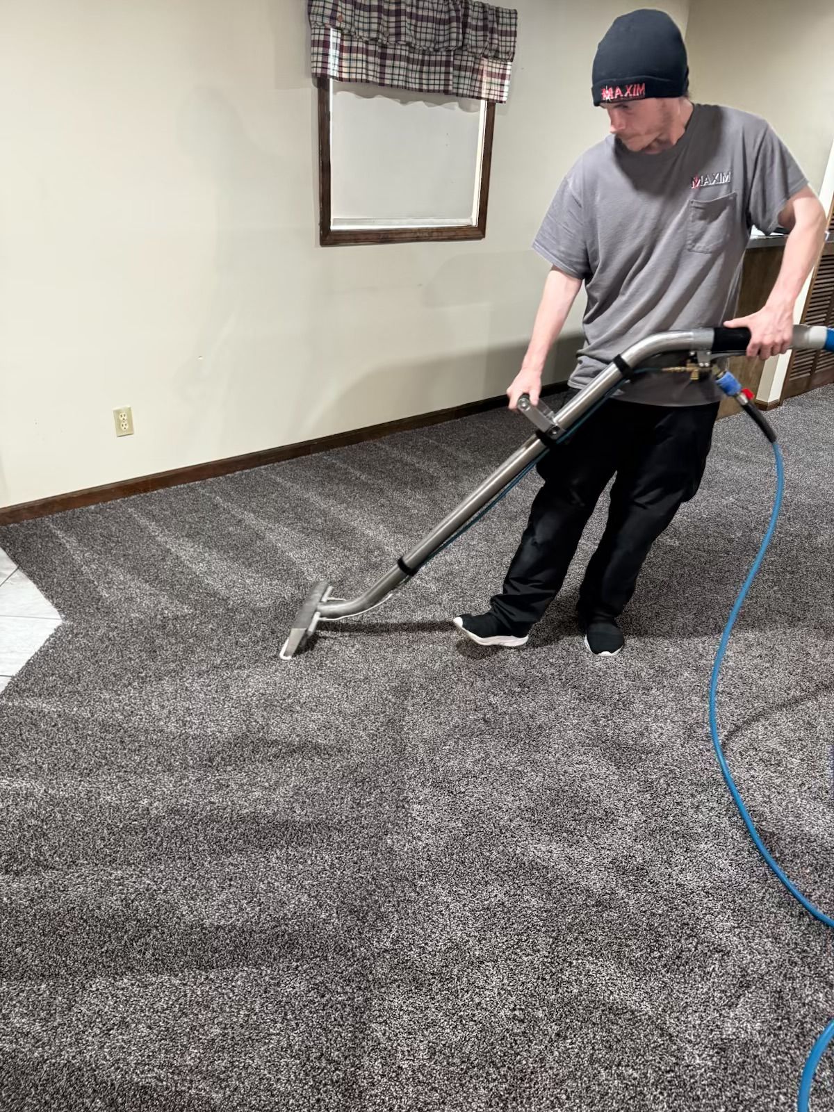 Person cleaning gray carpet with a machine, inside a room.