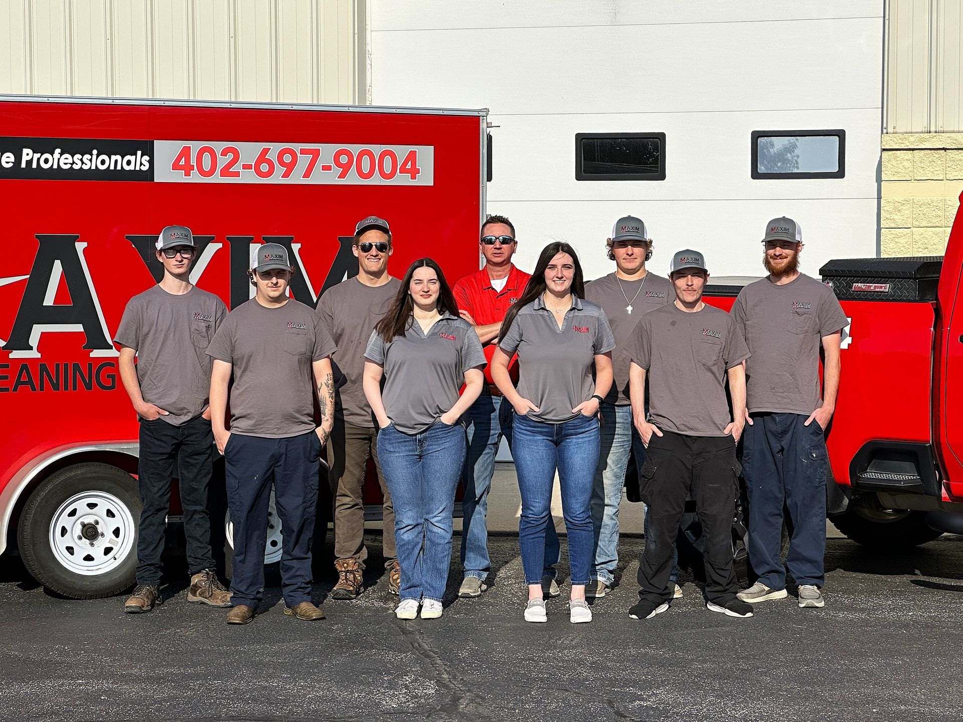 Group of people standing in front of a red truck and white trailer.